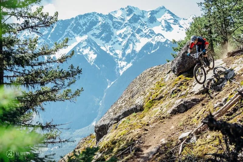 Rider su un sentiero roccioso sopra la valle con cime innevate alle spalle, nel corridoio Sea to Sky