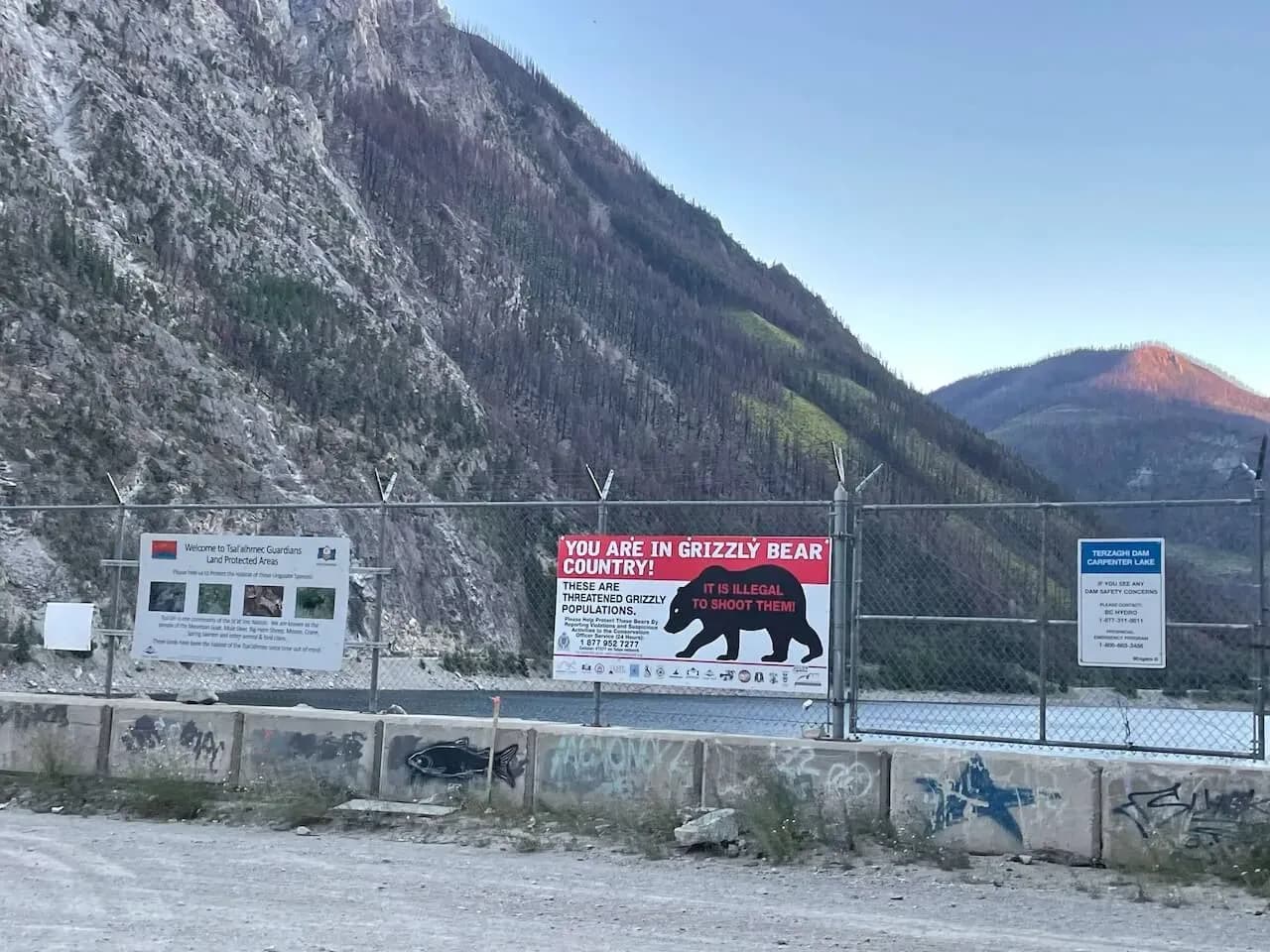 Cartelli di avviso per territorio di orsi grizzly su una recinzione a bordo strada, con montagne aride sullo sfondo