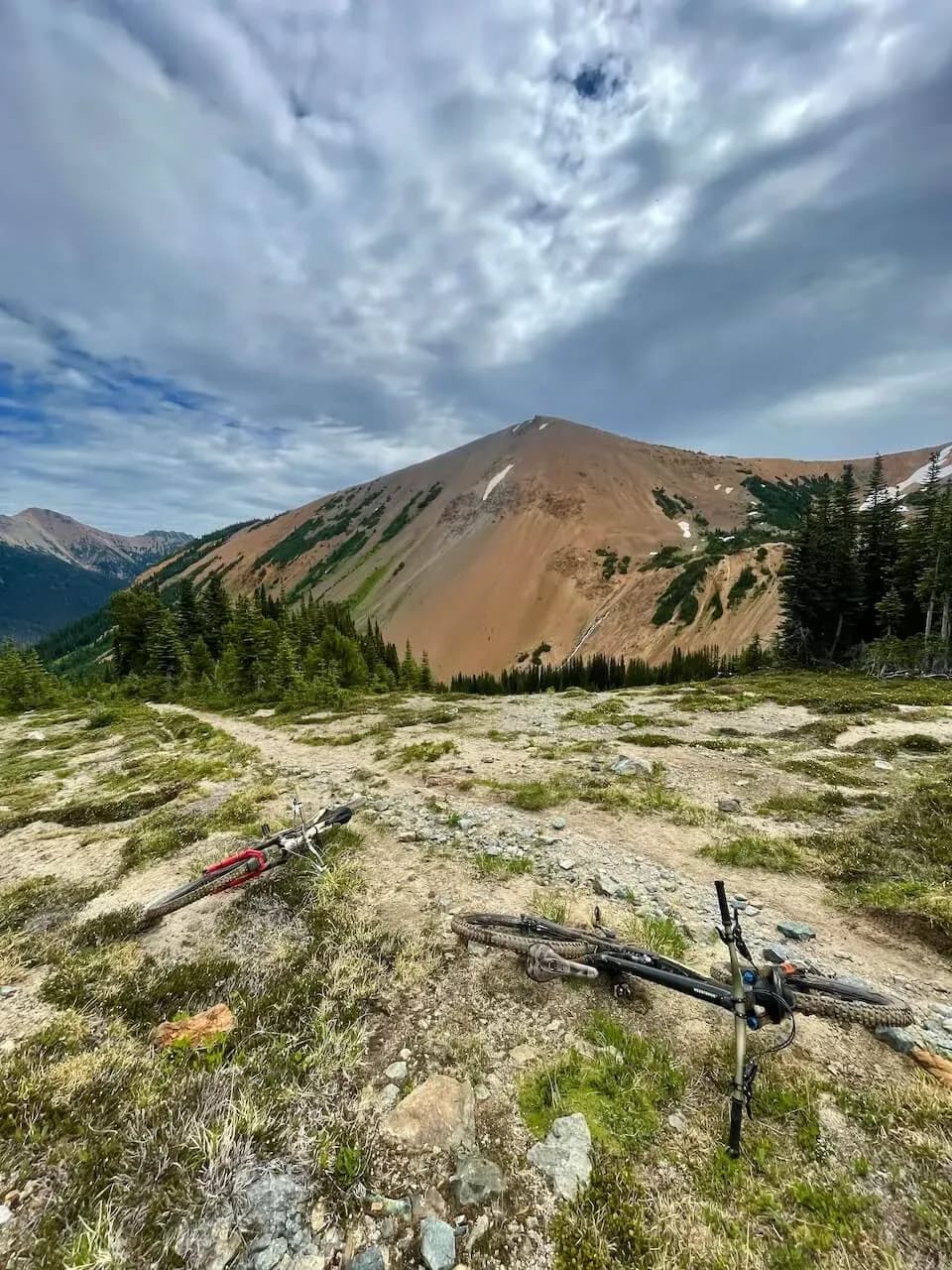 Mountain bike adagiata su un prato alpino sotto una cima rossastra nei South Chilcotins