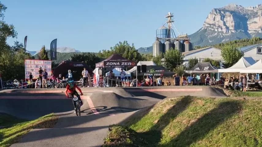 Rider on a pumptrack during a Zona Zero competition, with the public and mountains in the background