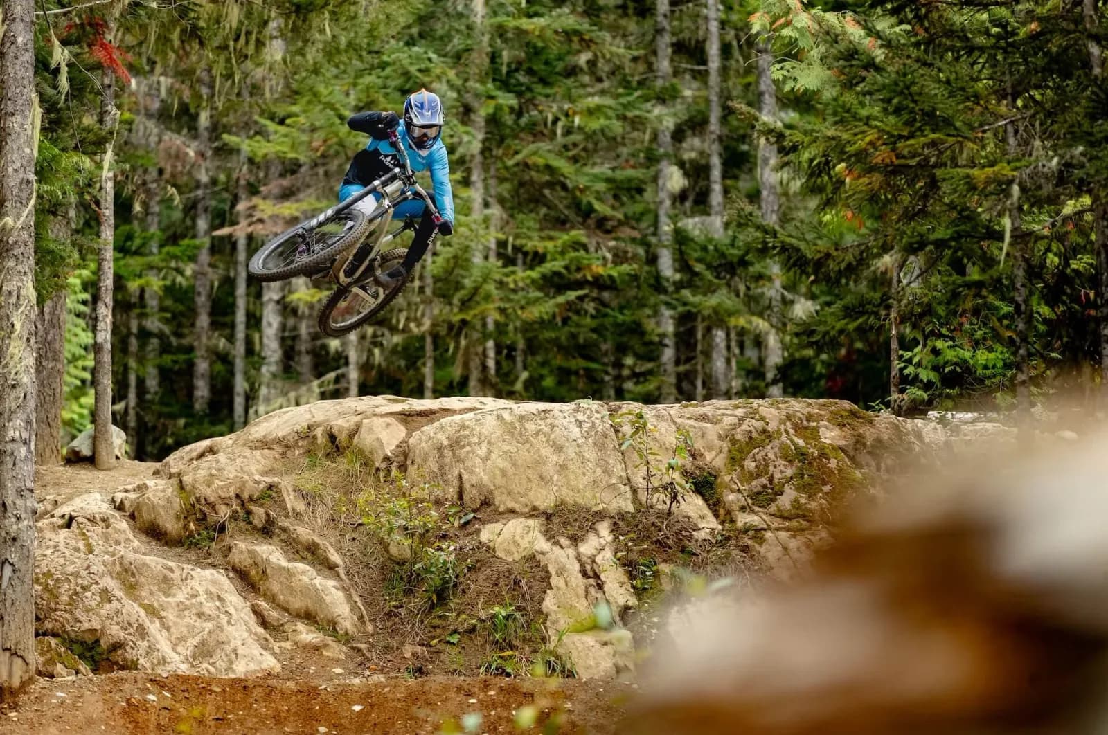 Rider jumping off a rock on A-Line, in the forest of Whistler Bike Park