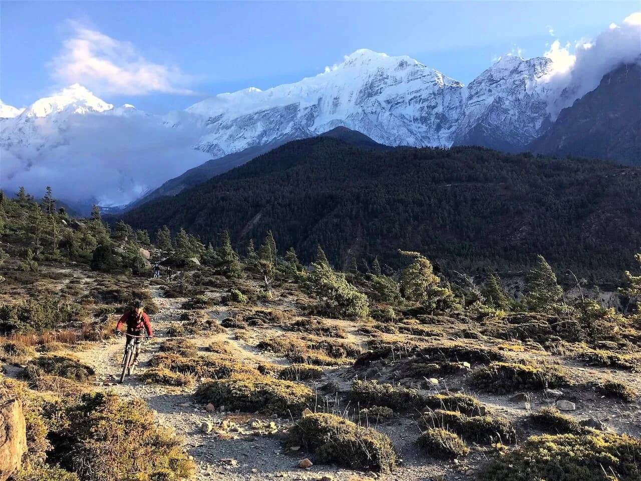 Mountainbiker auf einem steinigen Singletrail in Mustang, im Hintergrund schneebedeckte Gipfel des Himalaya