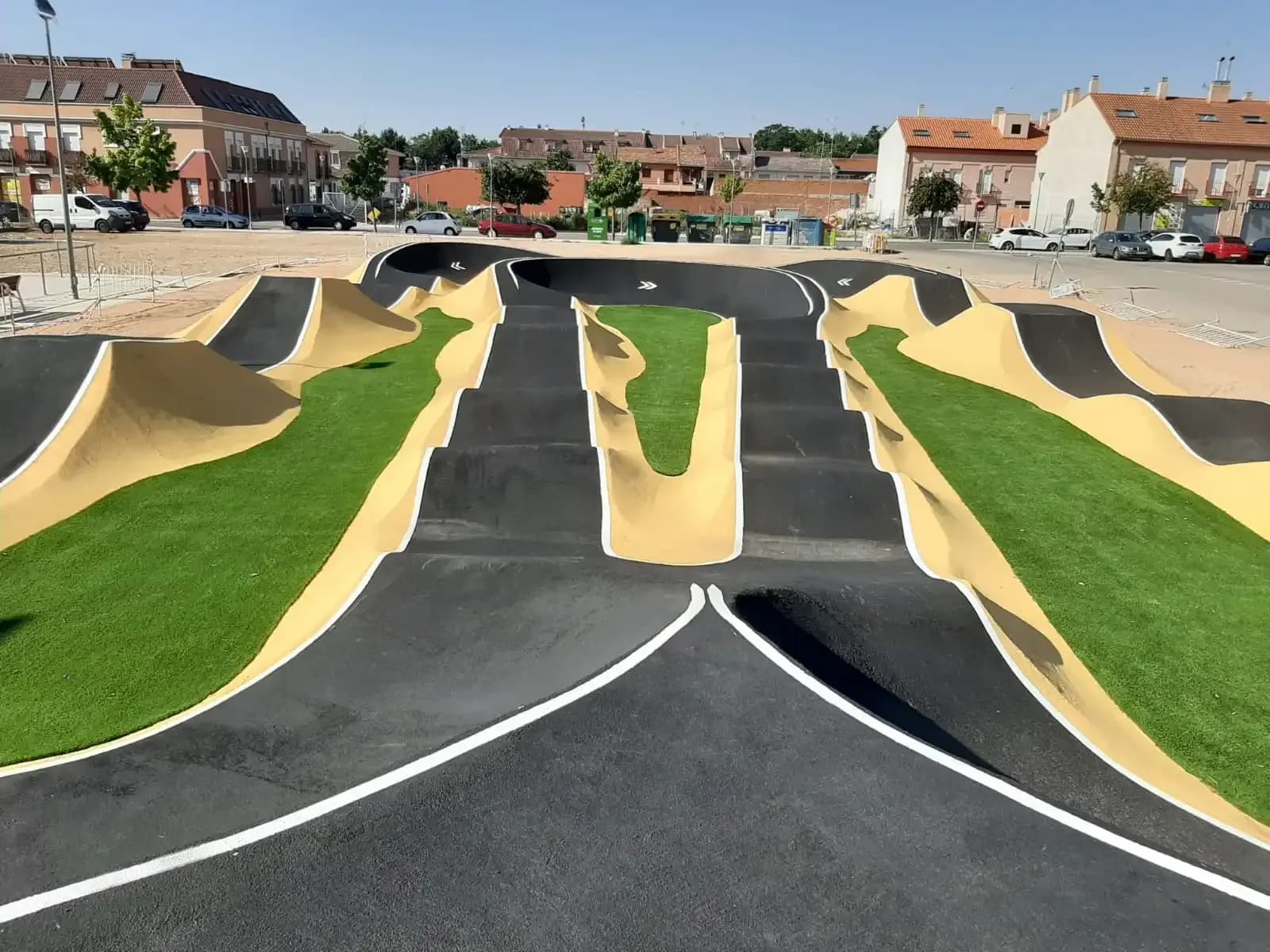 Asphalt-Pumptrack mit Steilkurven und Rollern zwischen Kunstrasen in einem spanischen Ort