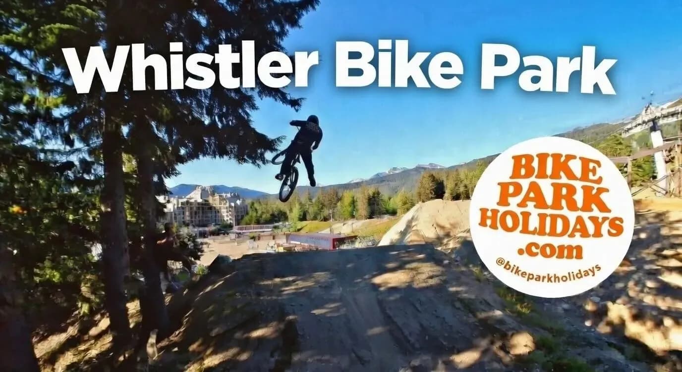 Rider in der Luft über einem Sprung im Whistler Bike Park, dahinter das Dorf und die Berge