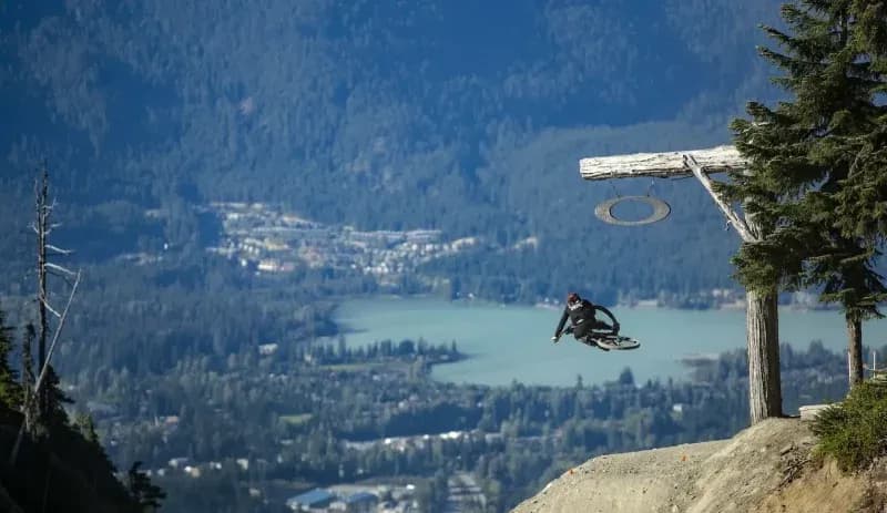 Rider in der Luft über einem Sprung im Whistler Bike Park, unten ein See und das Tal