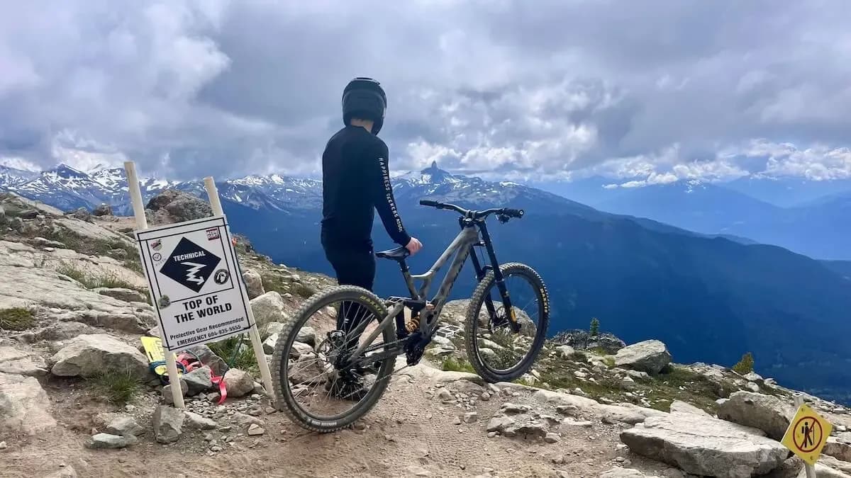 Rider mit seinem Bike neben dem Schild „Top of the World“ ganz oben im Whistler Bike Park